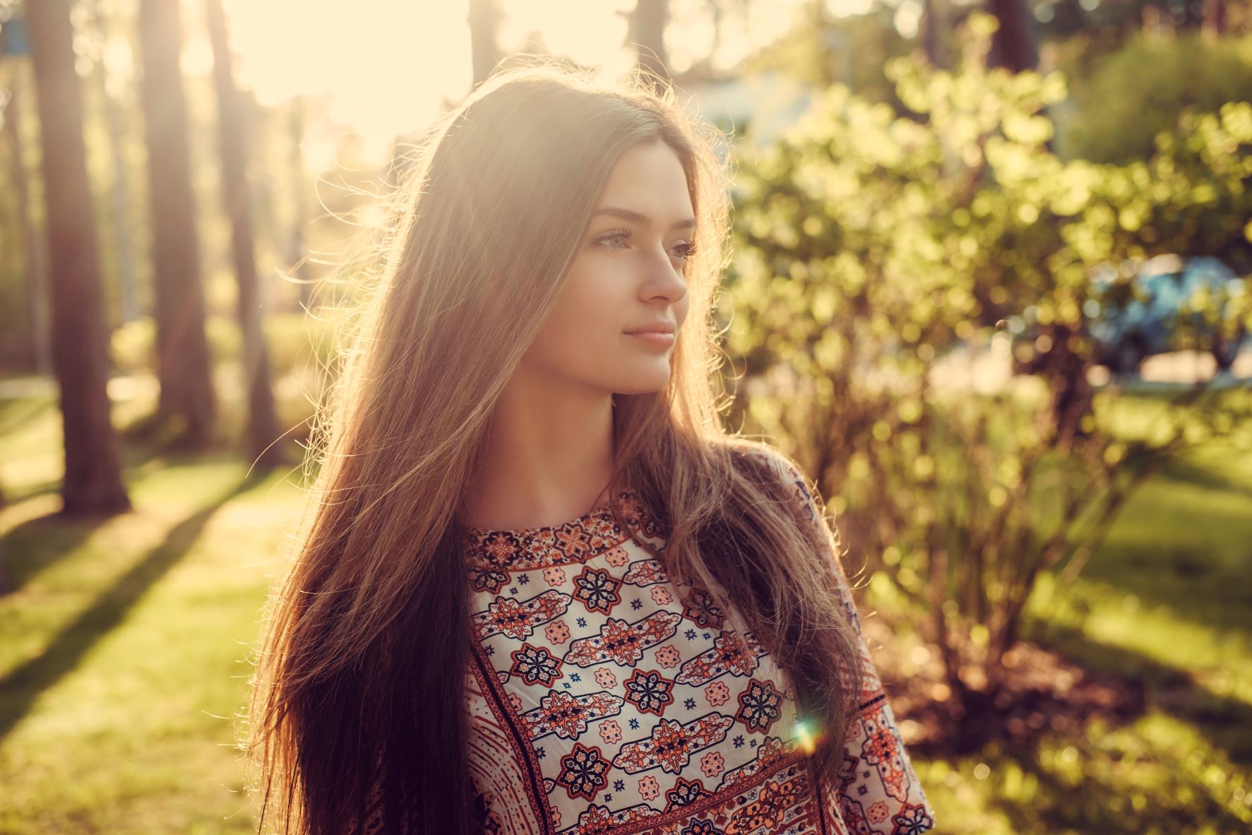 A woman with long hair that falls to mid-back standing outside in the sunlight
