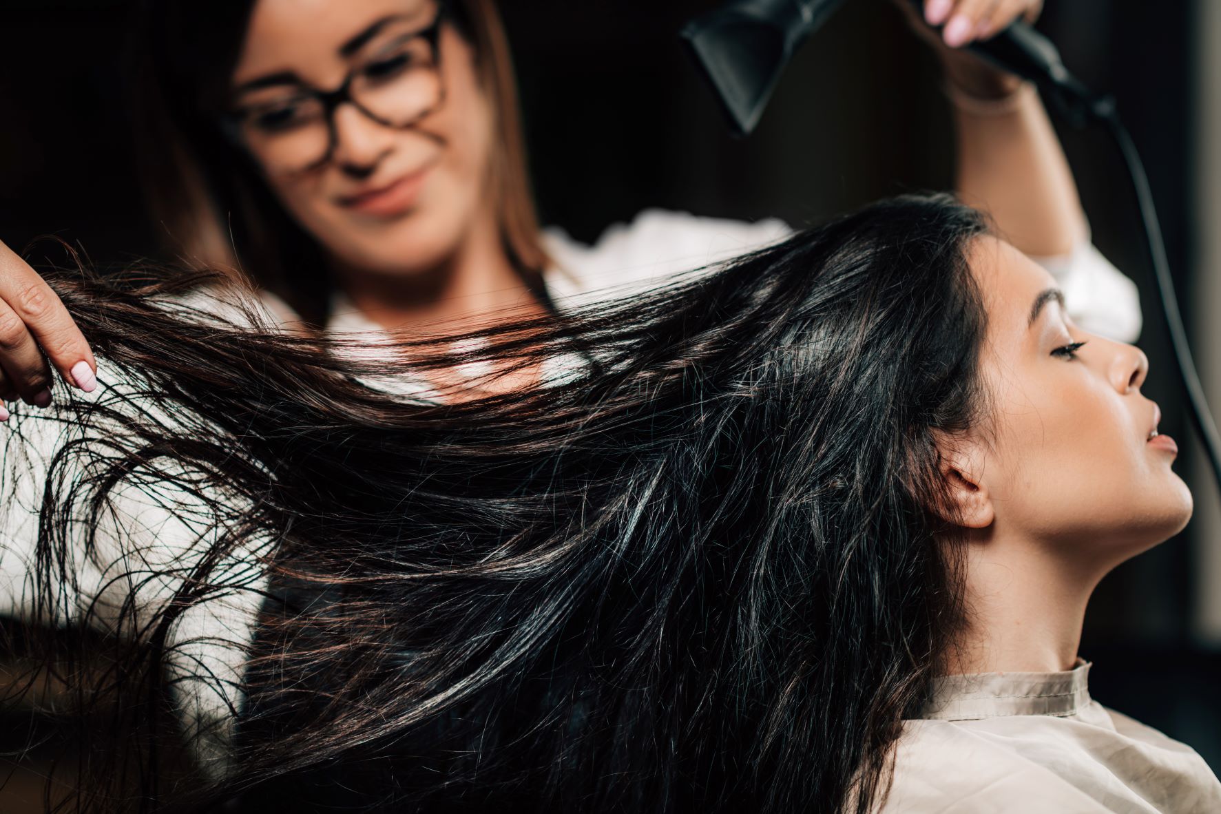 Hair stylist blow drying a woman's long, dark hair