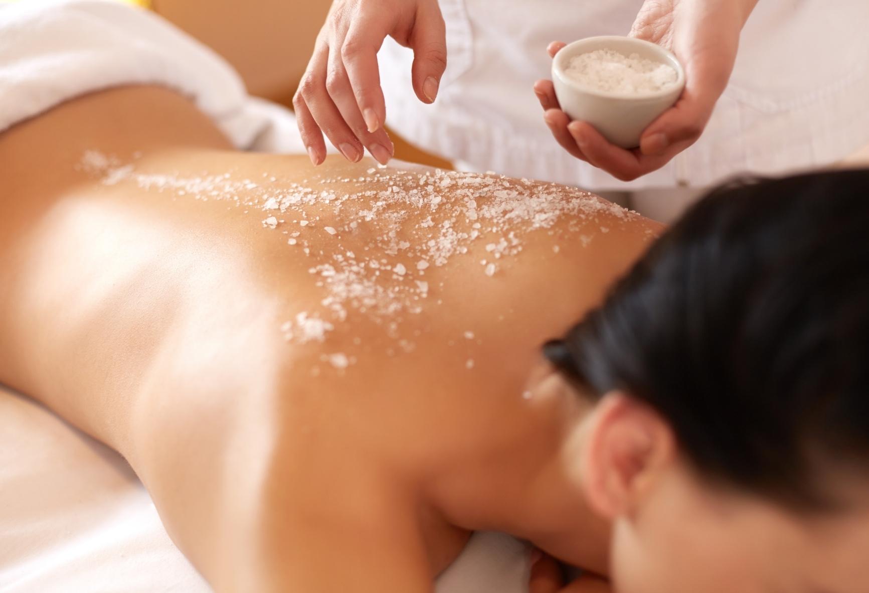Woman lying face down on massage table with salt scrub applied to her back