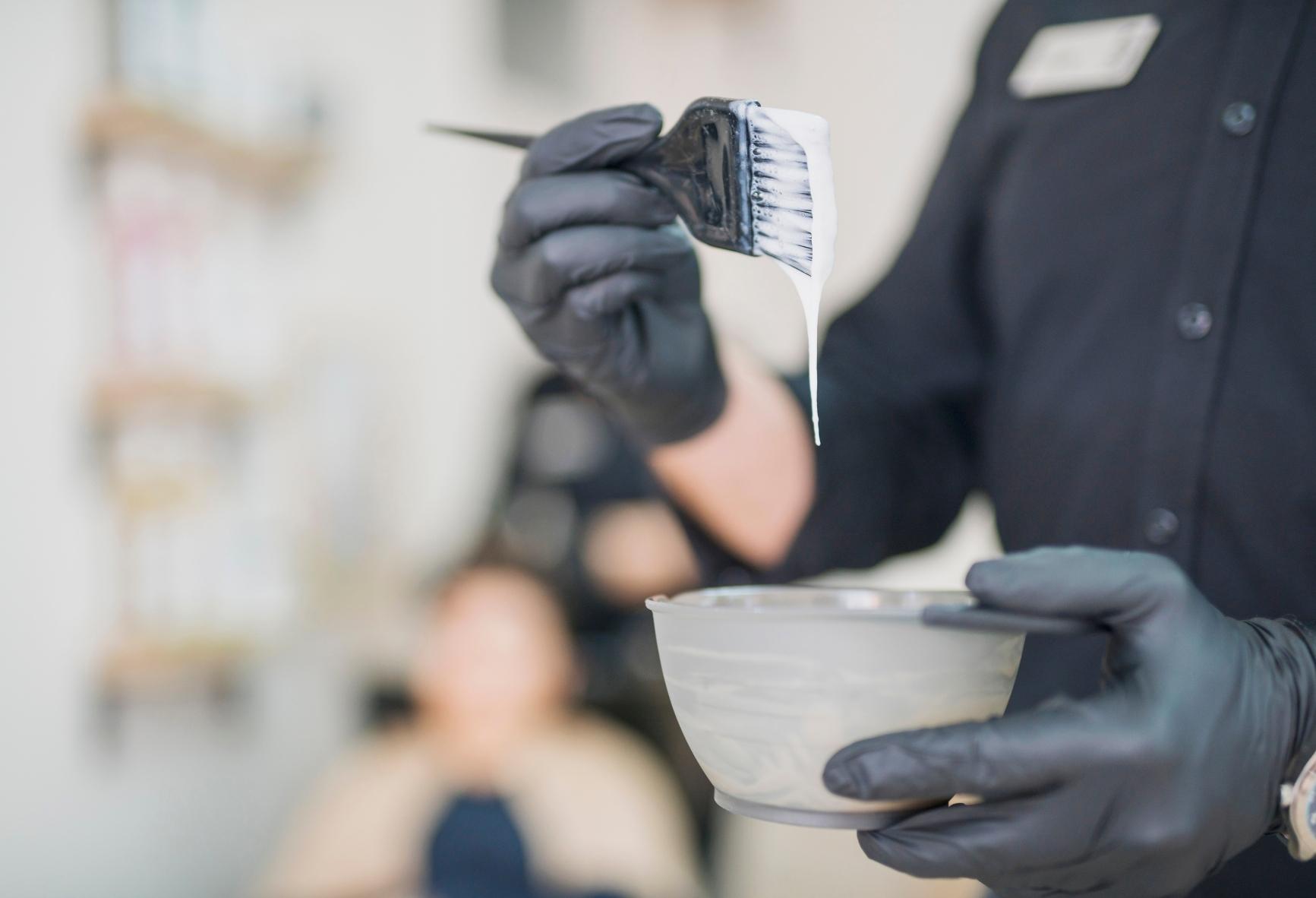 Hair stylist holds a brush with hair color above a small mixing bowl